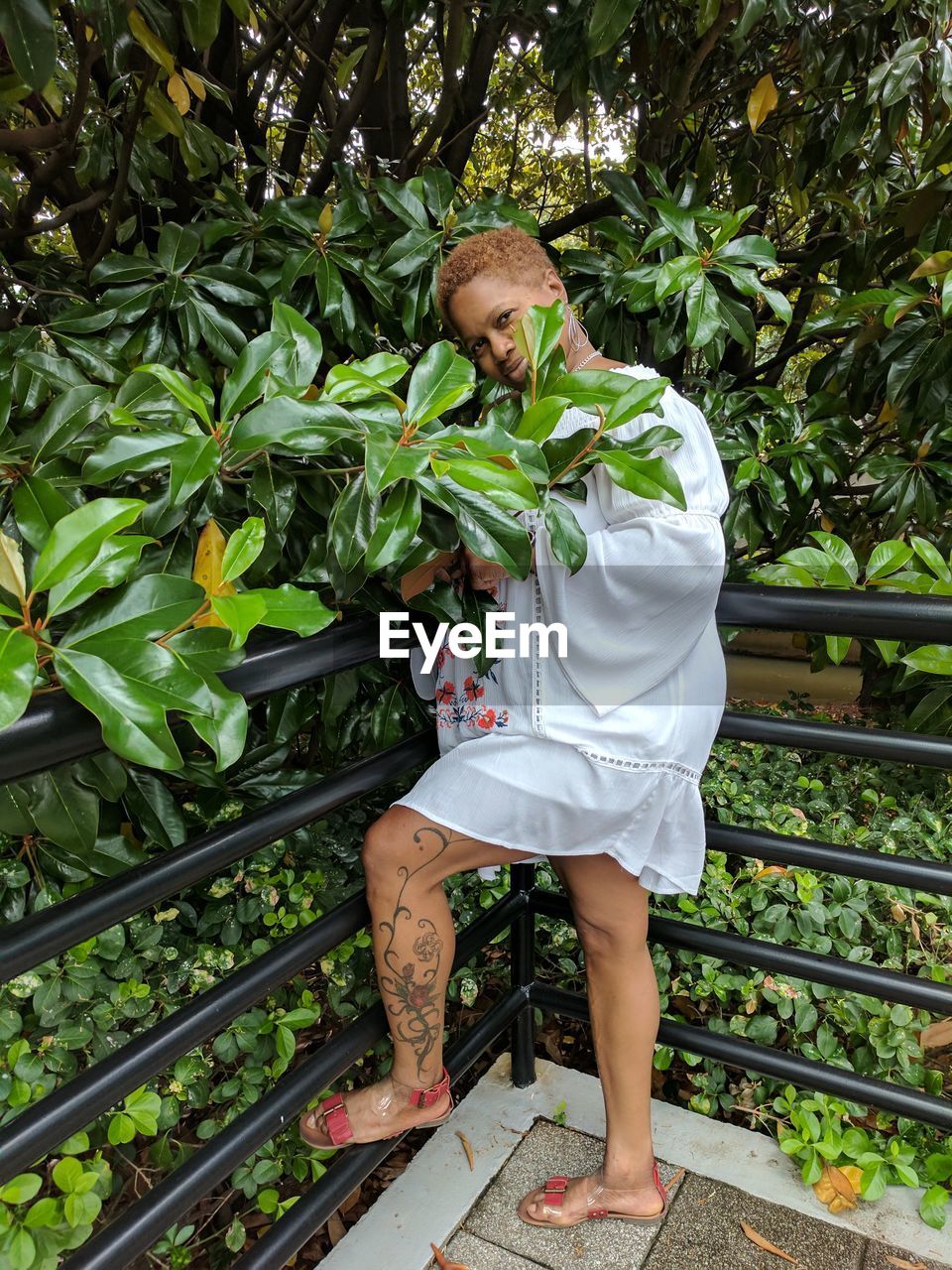 Portrait of woman standing by railing against plants