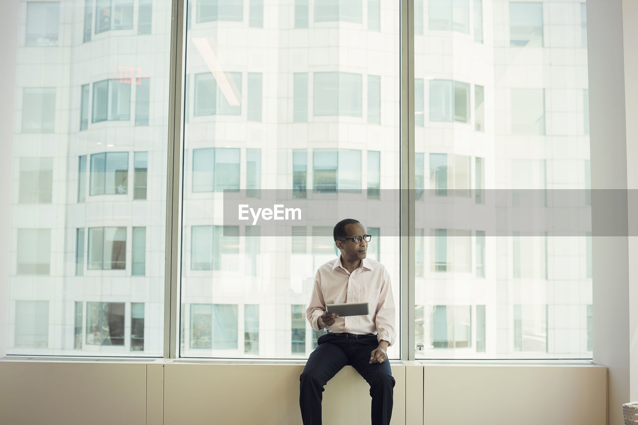 Businessman sitting on window sill holding digital tablet