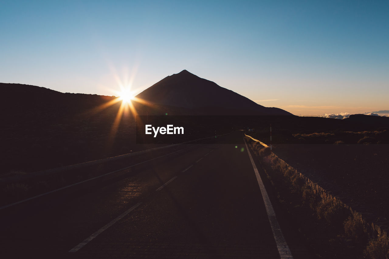 Road by silhouette mountain against sky during sunrise