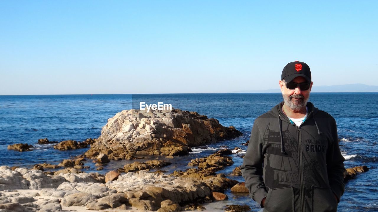 WOMAN STANDING ON ROCKS BY SEA