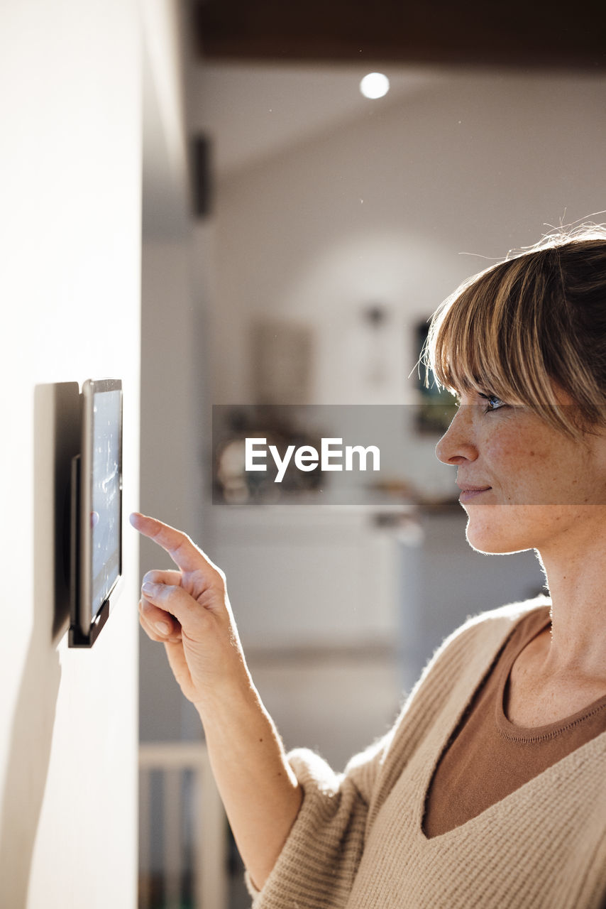 Woman touching tablet pc mounted on wall at home