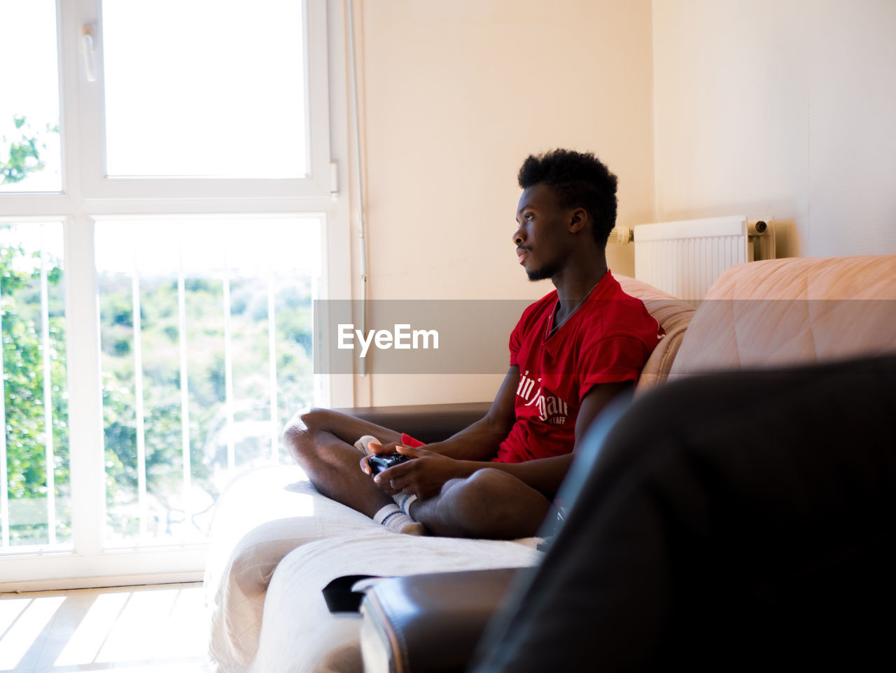 Young man using wireless playstation pad while sitting on bed at home
