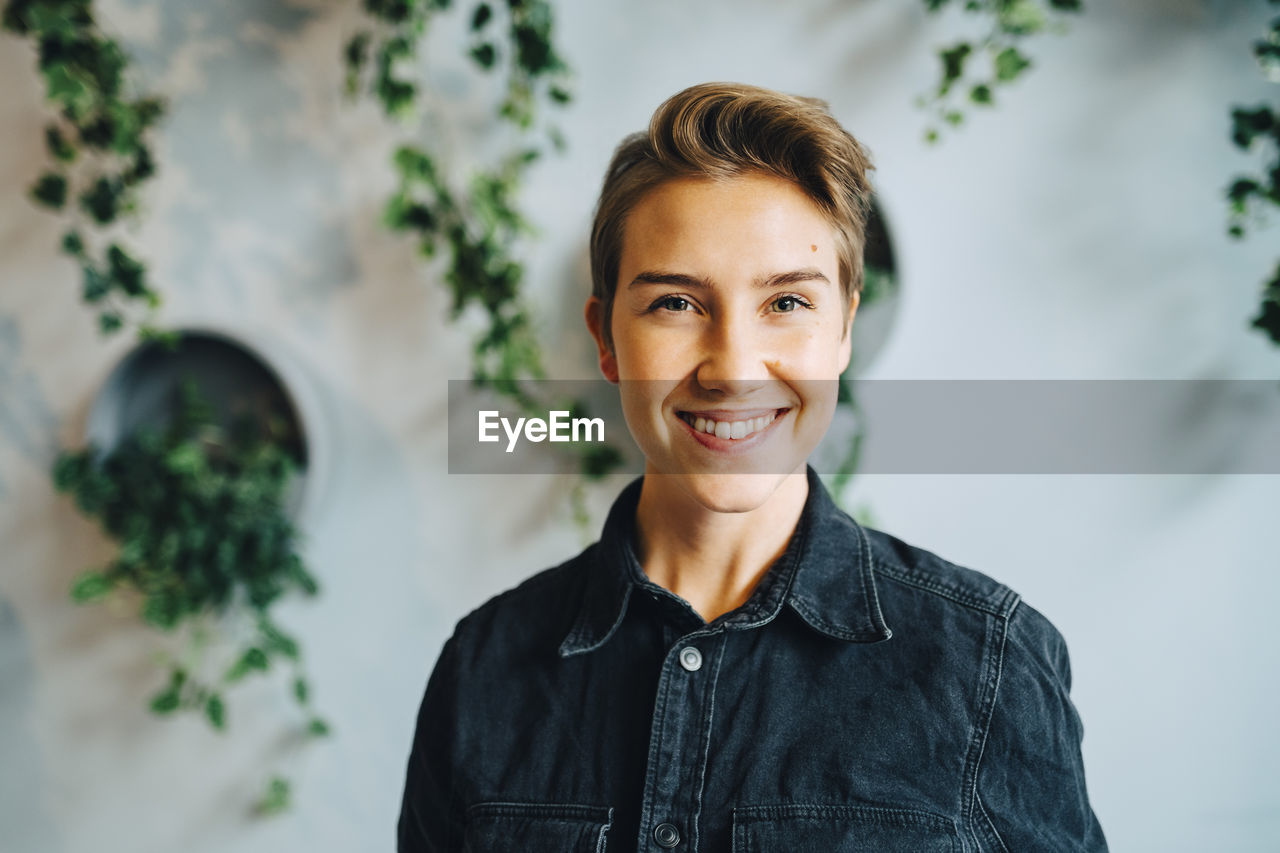 Portrait of smiling female entrepreneur against wall in office