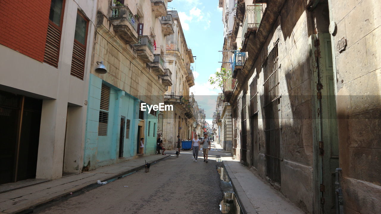 MAN WALKING ON FOOTPATH AMIDST BUILDINGS