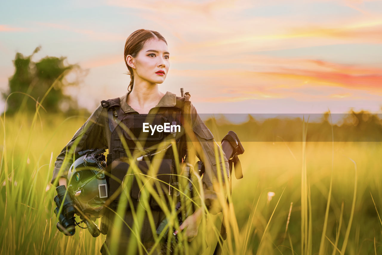 Young woman looking away while standing on field against sky