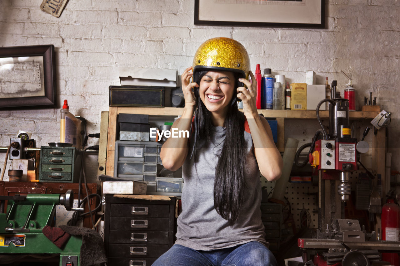 Cheerful female owner wearing helmet in auto repair shop