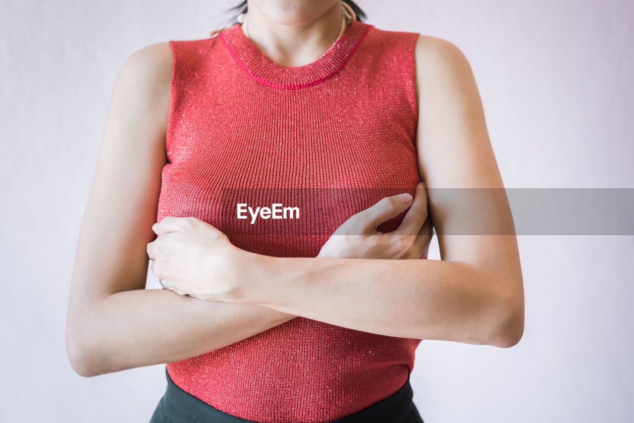 Midsection of woman touching breast while suffering from cancer while standing against white background