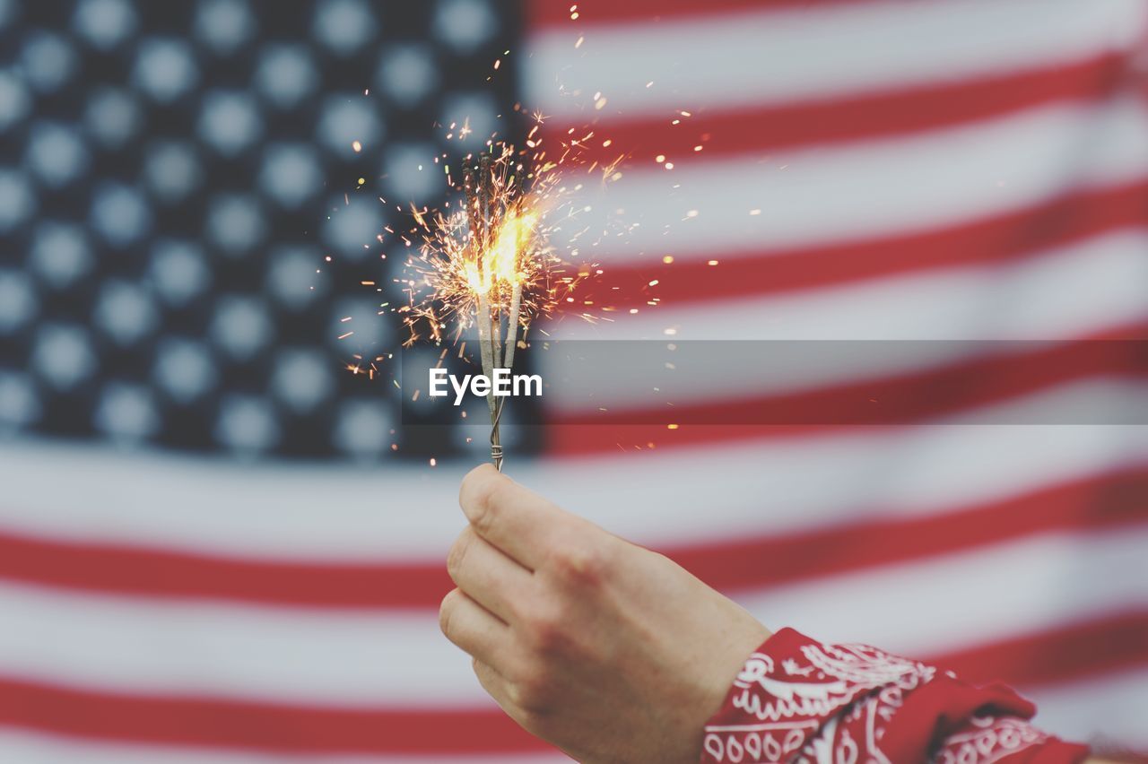 Cropped hand holding illuminated sparkler against american flag