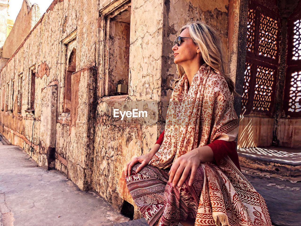 Mature woman wearing sunglasses and traditional clothing sitting against old building