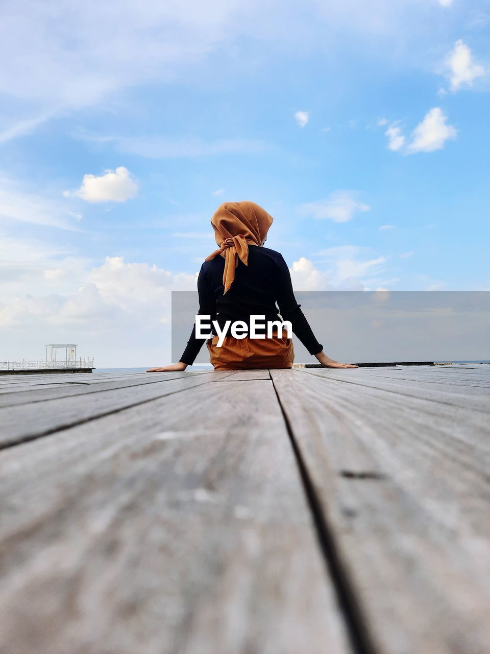 Woman sitting on pier against sky