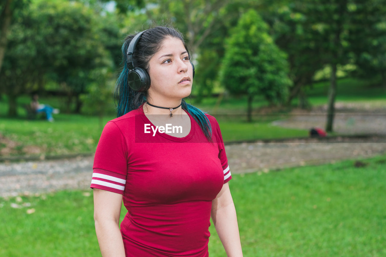 Beautiful college woman with blue hair and red dress listening to music with her wireless headphones