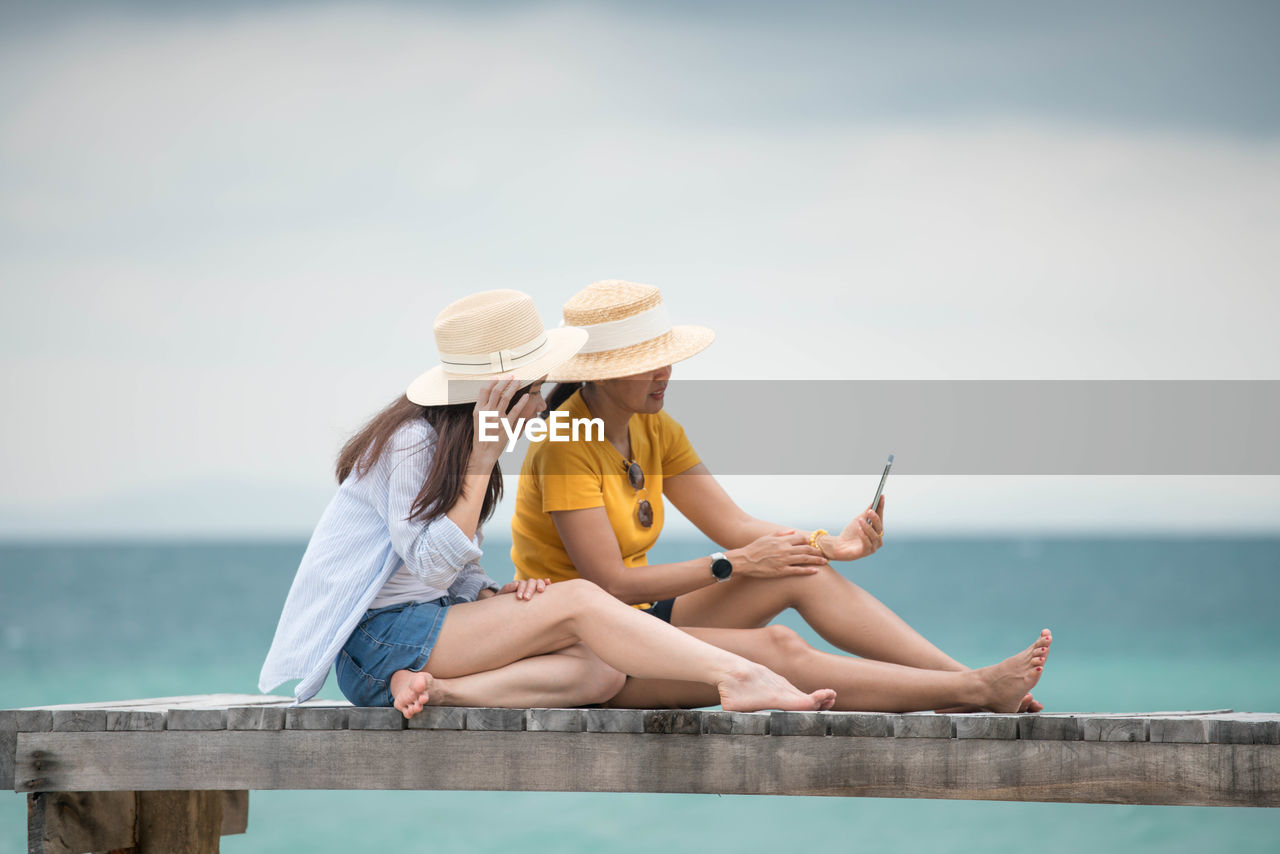 Woman sitting on deck chair by sea against sky