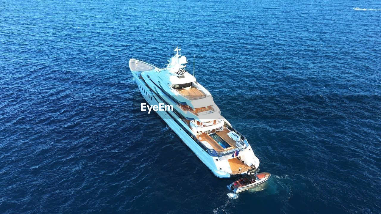 Superyacht with pool and helicopter landing space, in the water with its tender