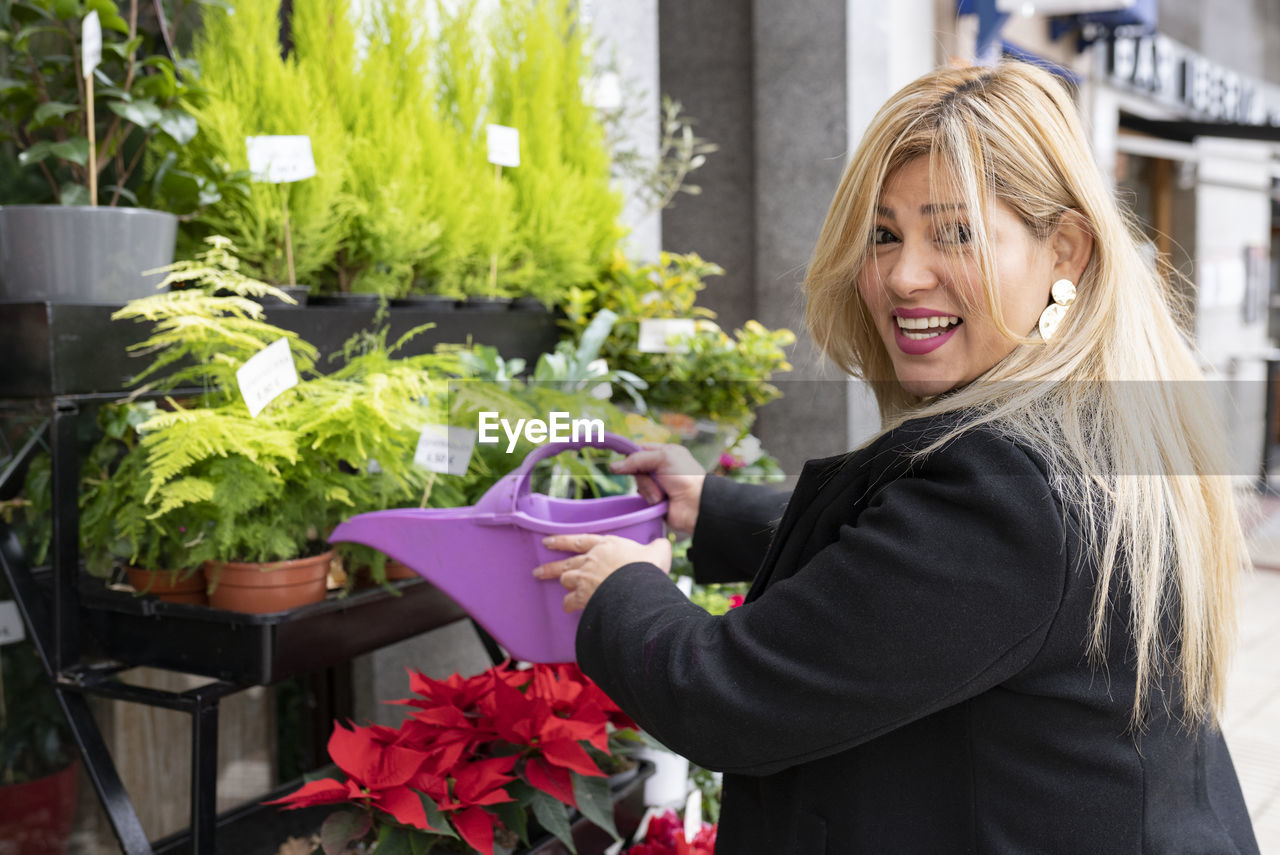 Smiling florist watering plants outside flower shop