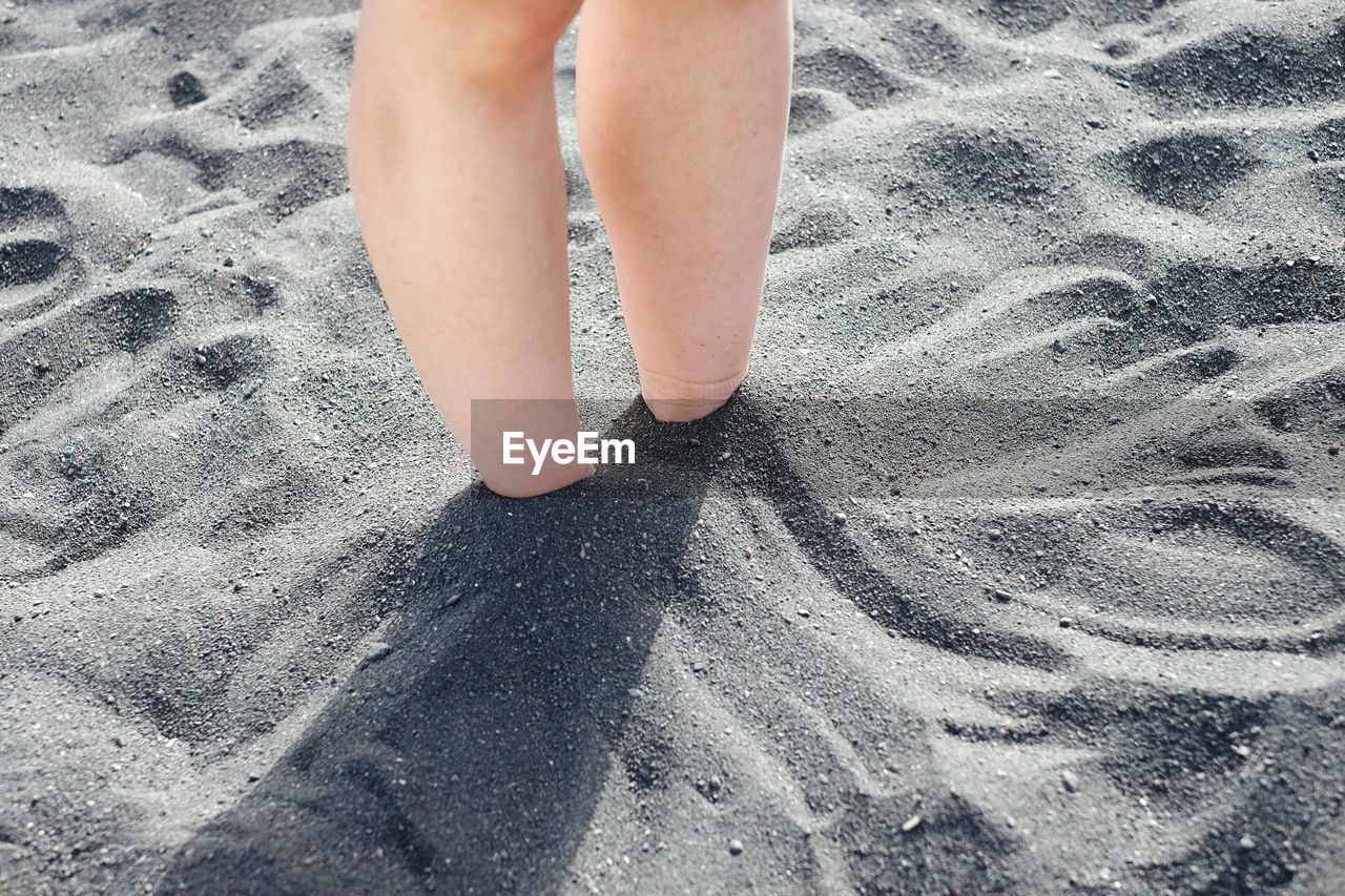 Close-up low section of bare legs in sand