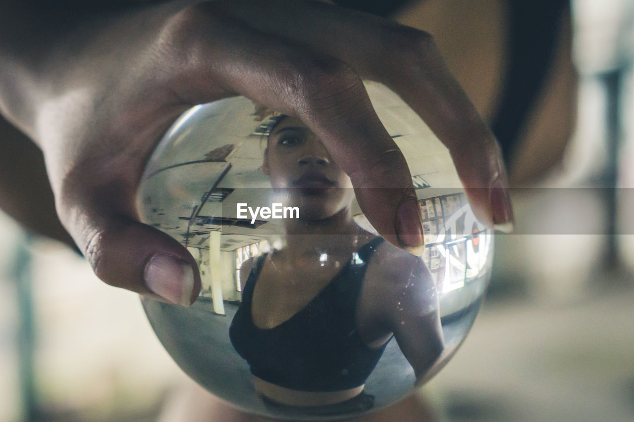 Cropped hand touching crystal ball with reflection of woman