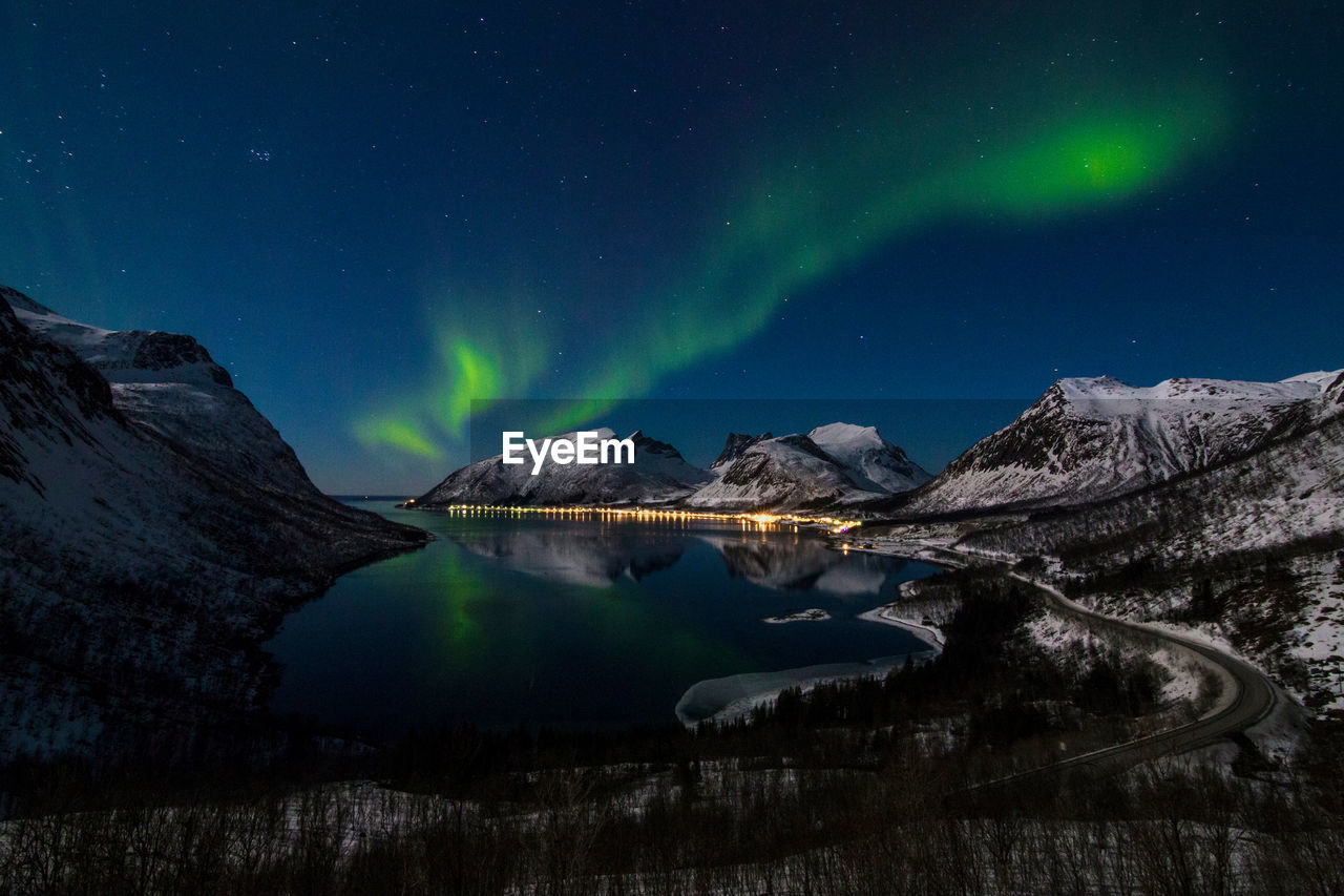 Northern lake at night view to northern leafless forest in winter under starry cloudless sky with polar light.