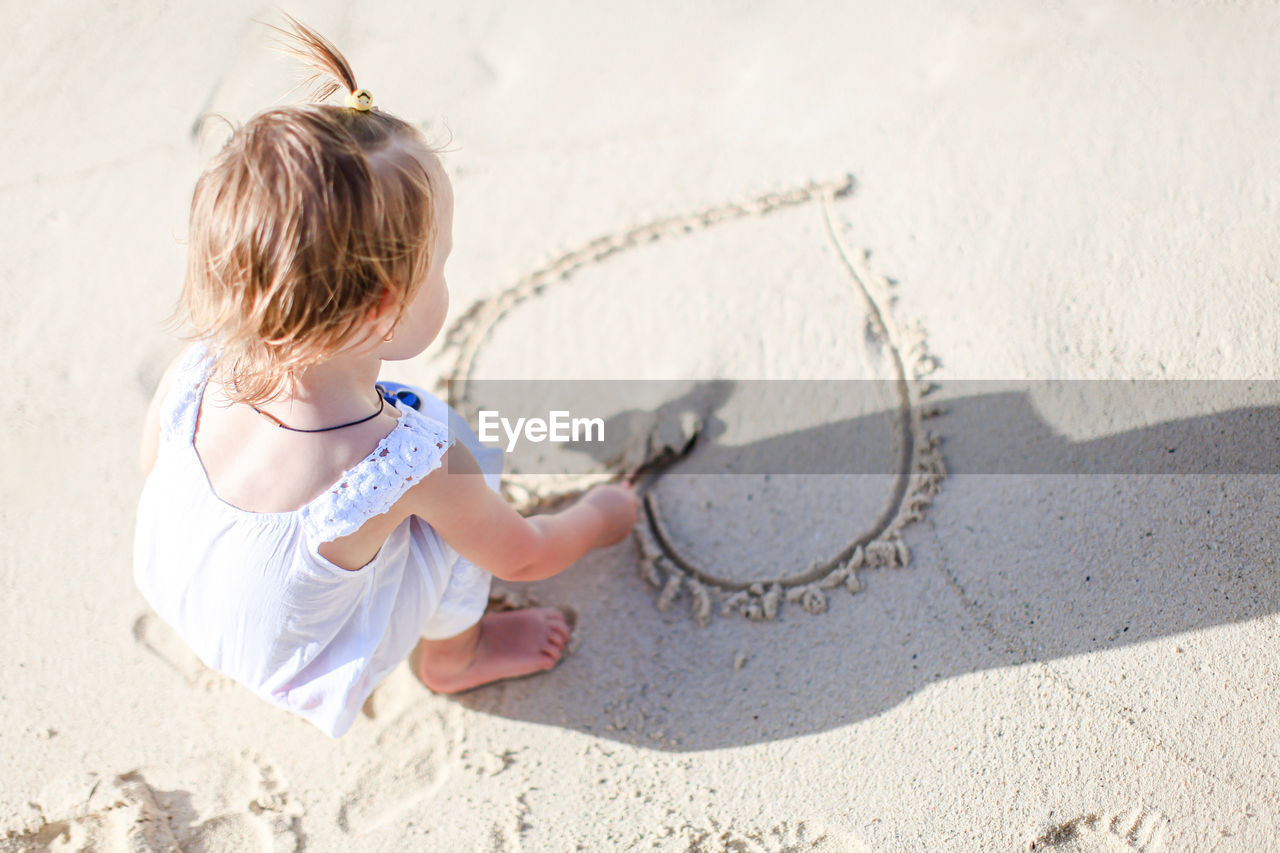 High angle view of girl making heart shape on sand at beach