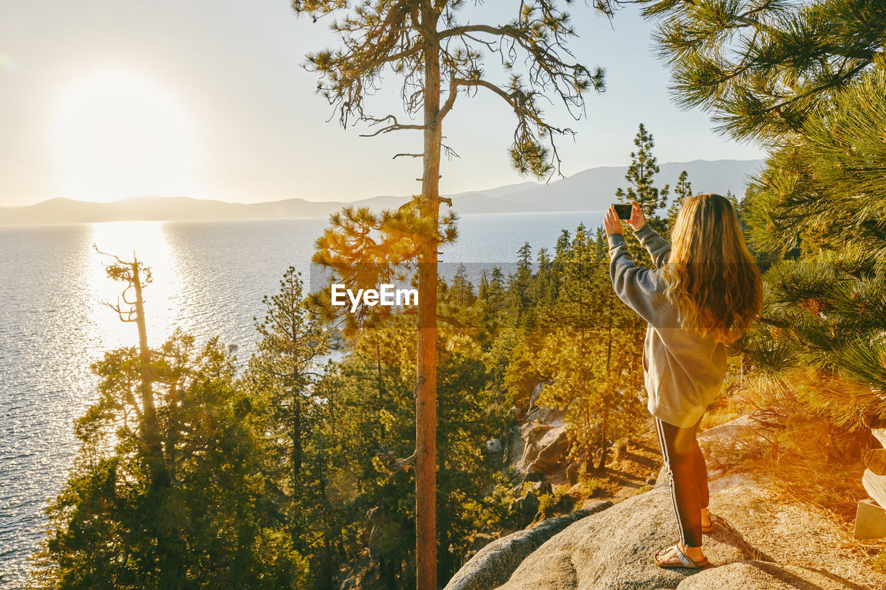 Young woman taking a picture of sunset over lake tahoe.