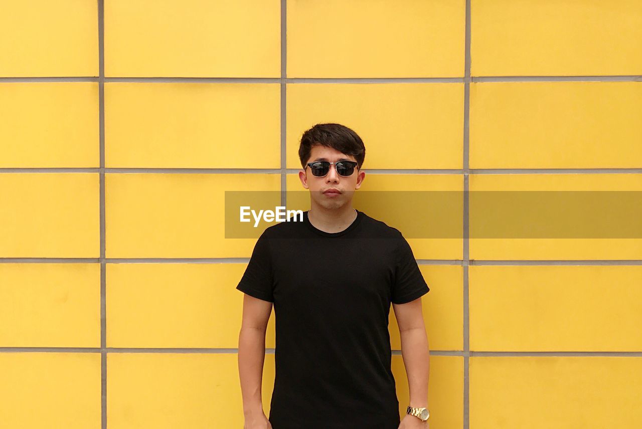 Portrait of young man standing against yellow wall