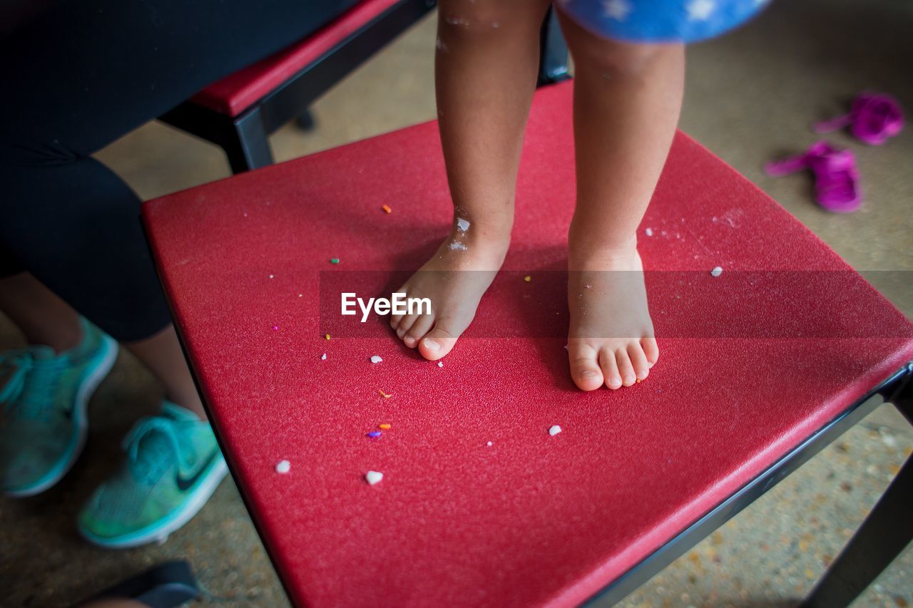 Low section of child standing on red stool at home