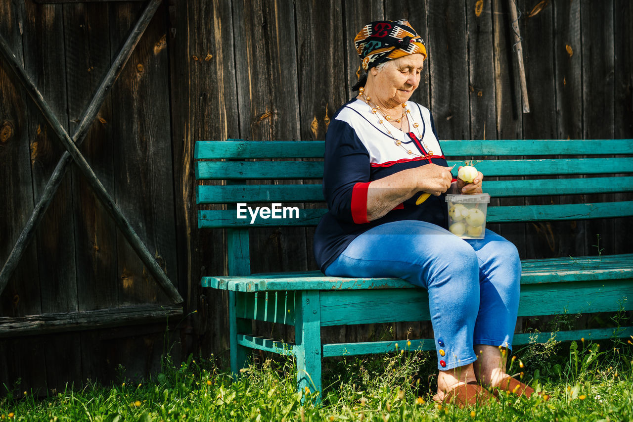 Senior woman peeling apple while sitting on bench at park