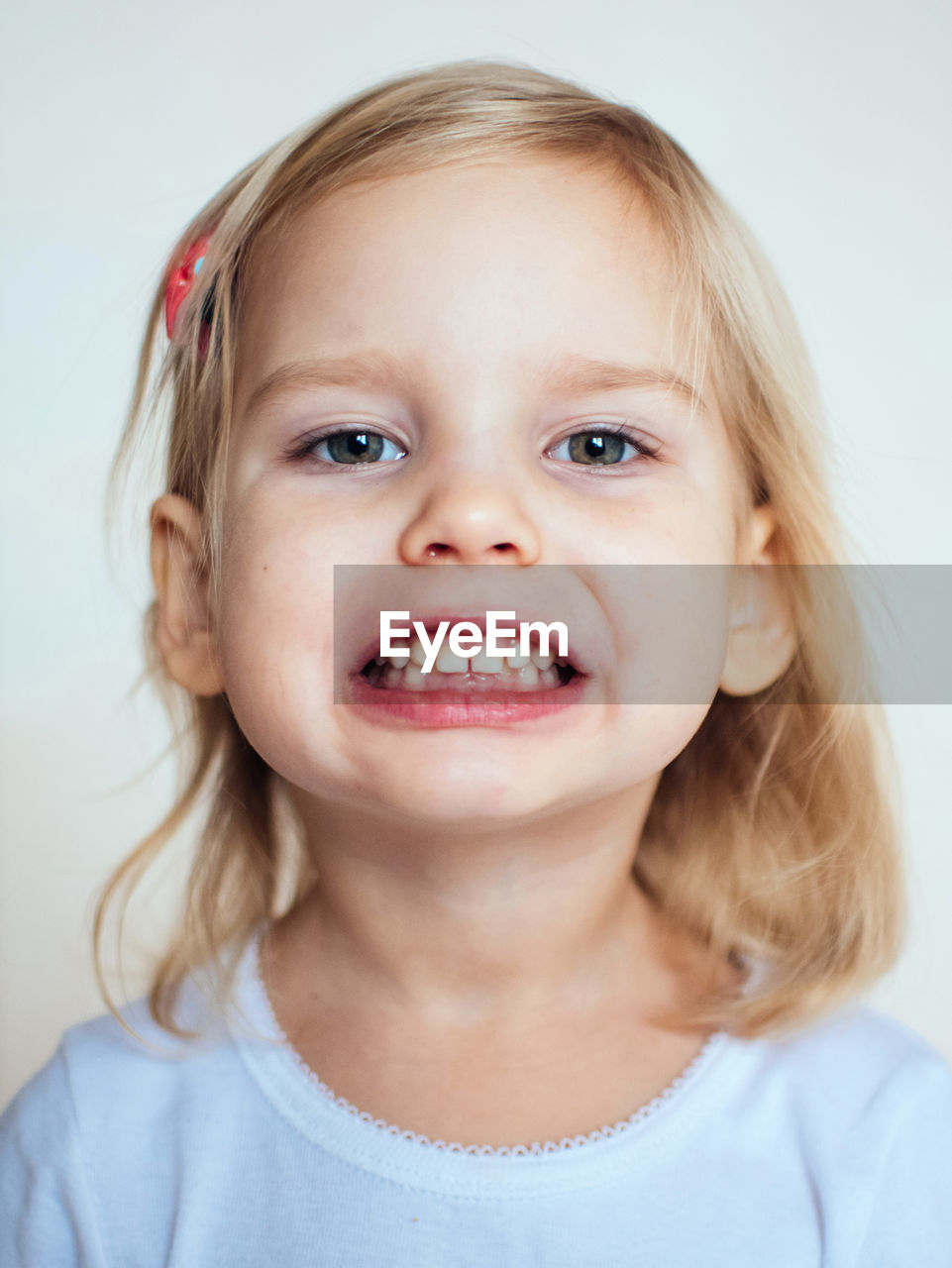 Portrait of cute girl clenching teeth against white background