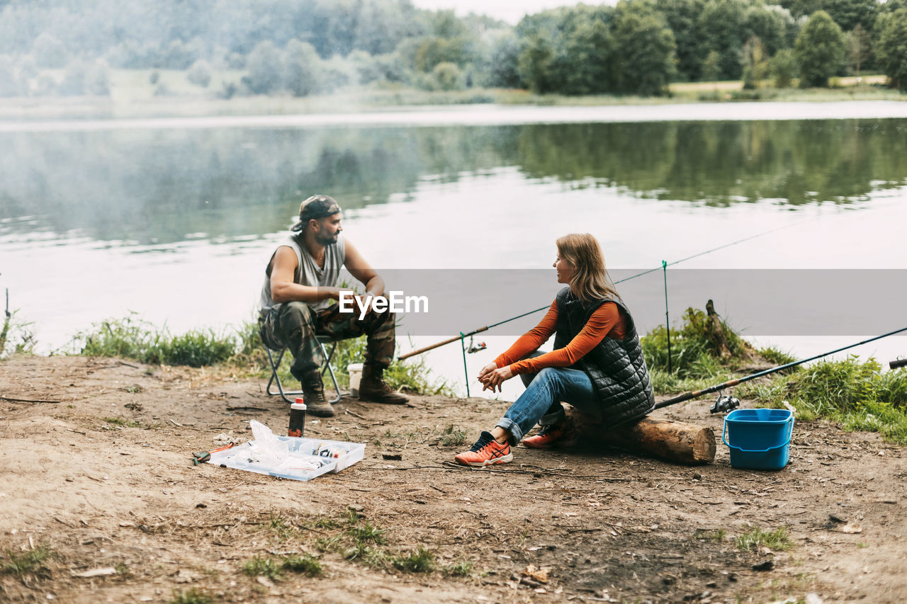 A man and a woman are fishing on the shore of a lake or river. a married couple spends time together