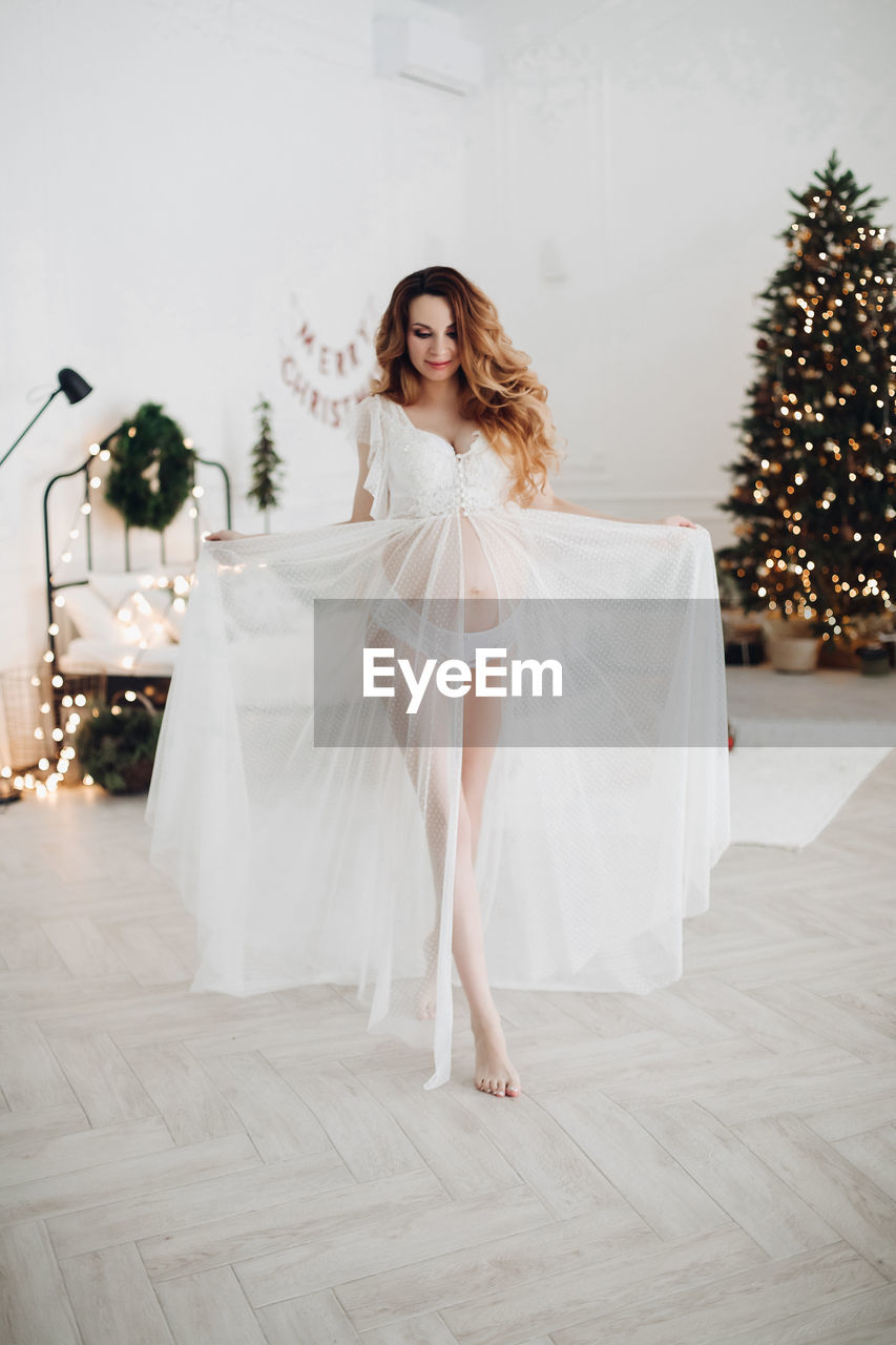 Young woman wearing dress against christmas tree