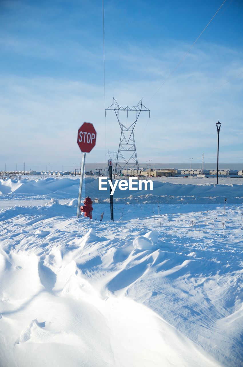 Stop sign on snow covered field against sky