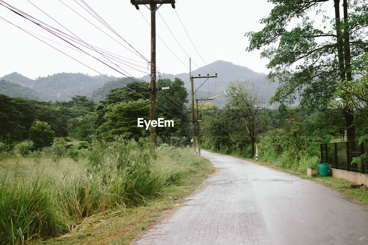 ROAD AMIDST TREES AND MOUNTAINS AGAINST CLEAR SKY