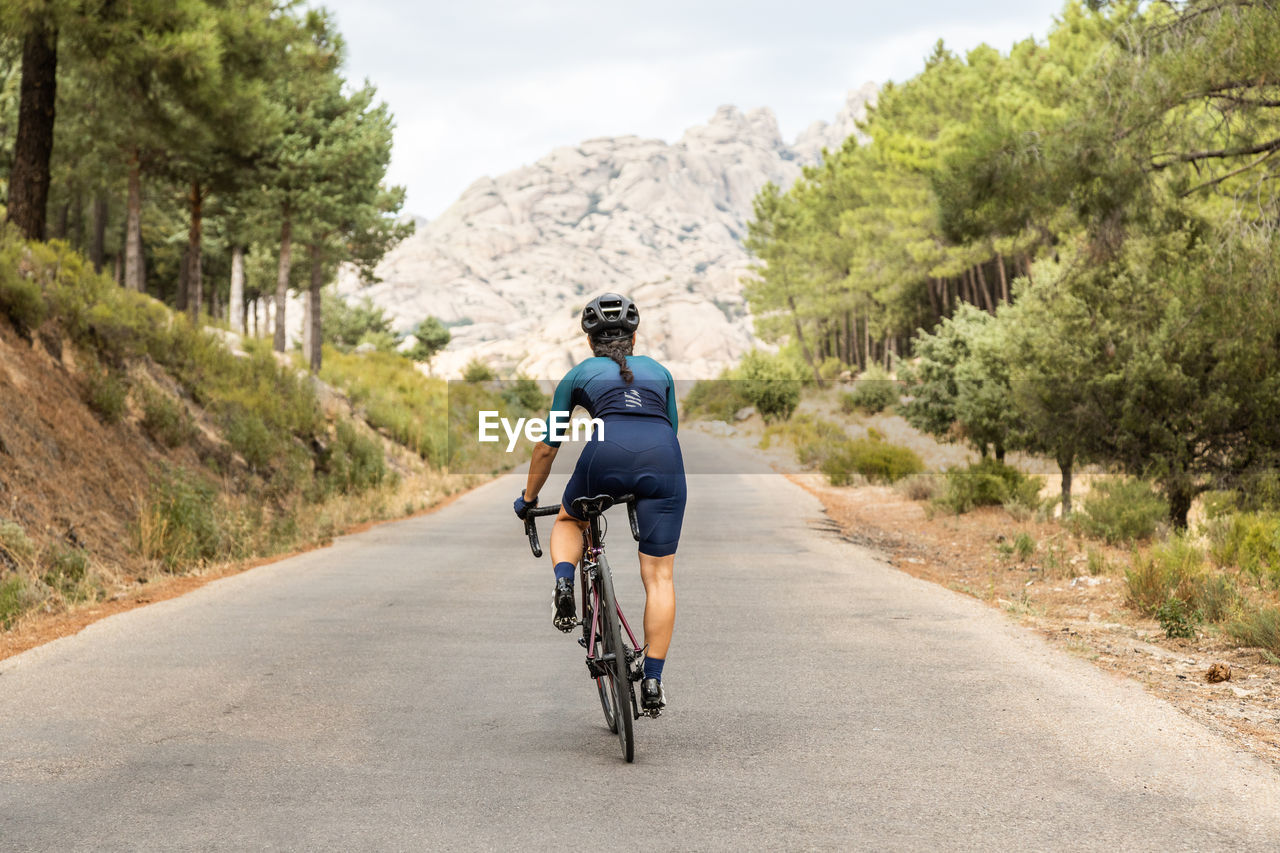 Mature woman training road bike, climbing a mountain road, back view