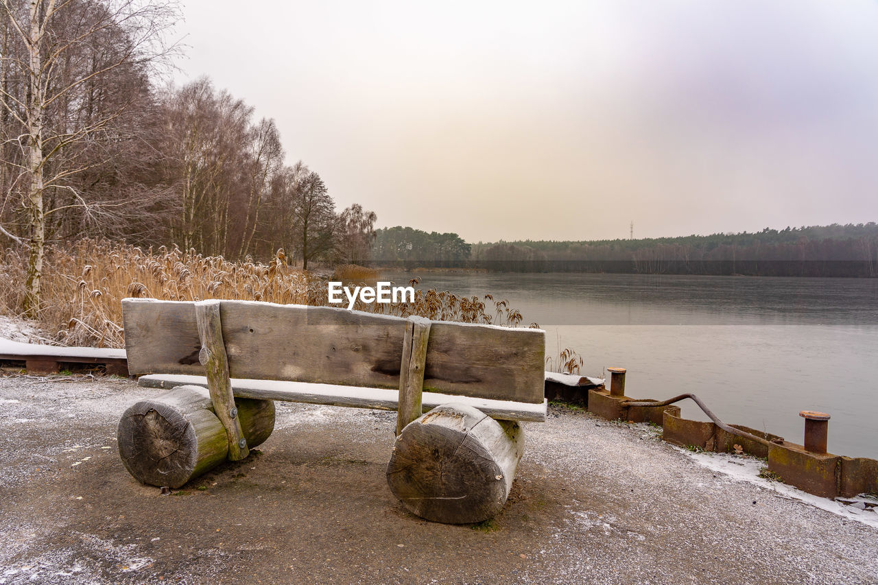 EMPTY BENCH BY LAKE AGAINST SKY