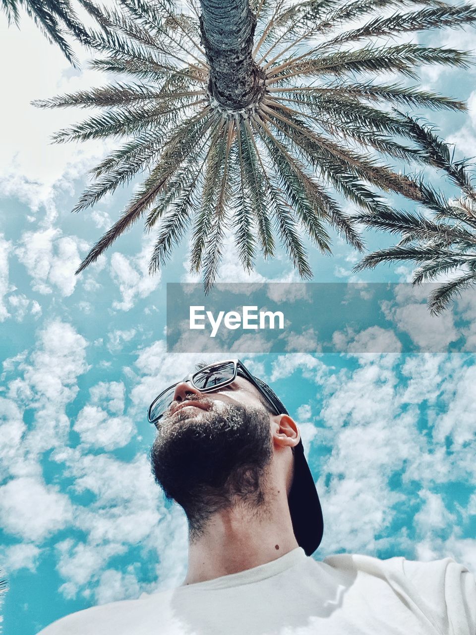 Low angle view of bearded man and palm trees against cloudy sky