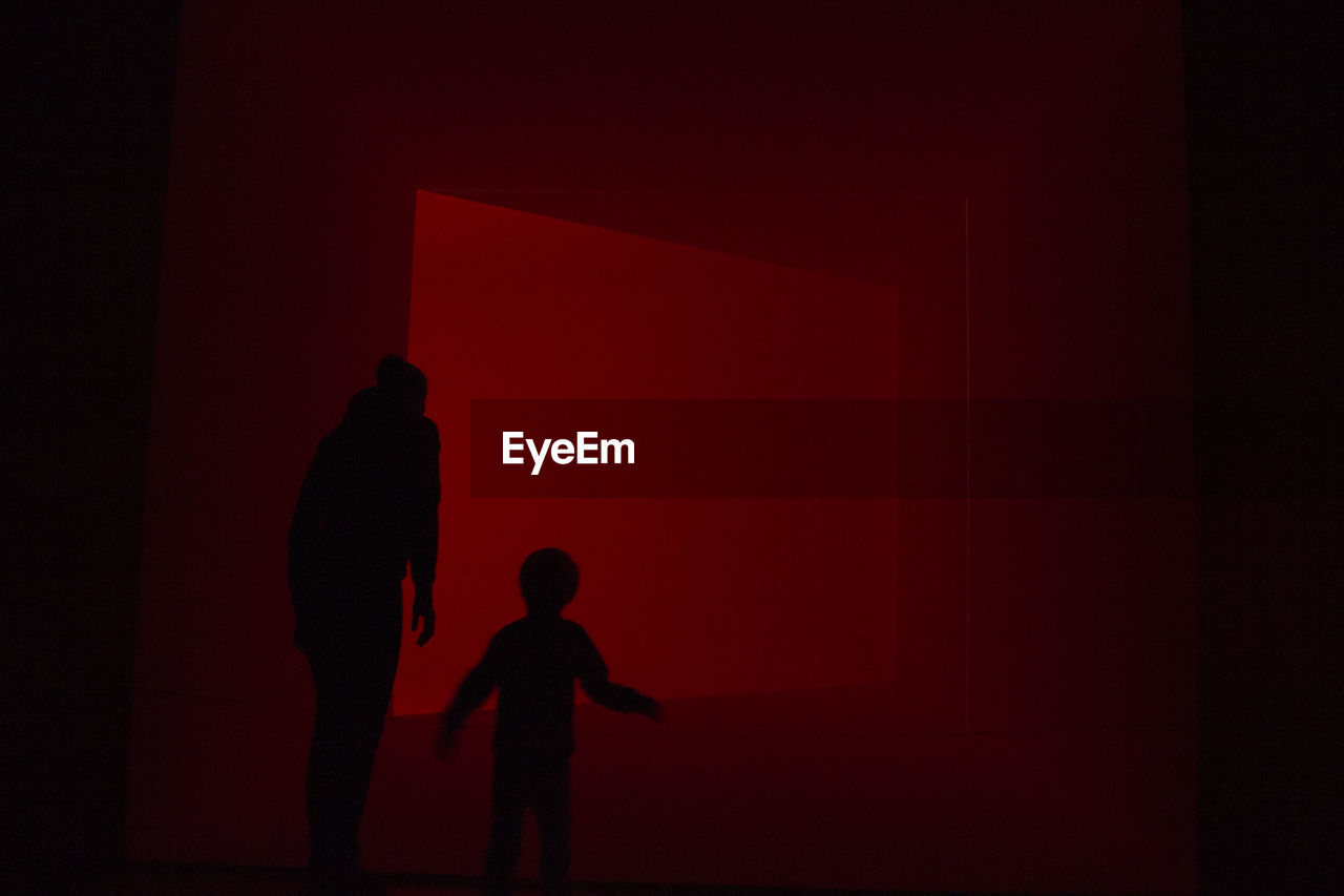 SILHOUETTE OF CHILD STANDING IN RED LIGHT