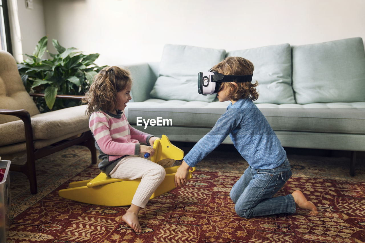 Boy wearing virtual reality simulator playing with sister sitting on rocking horse at home