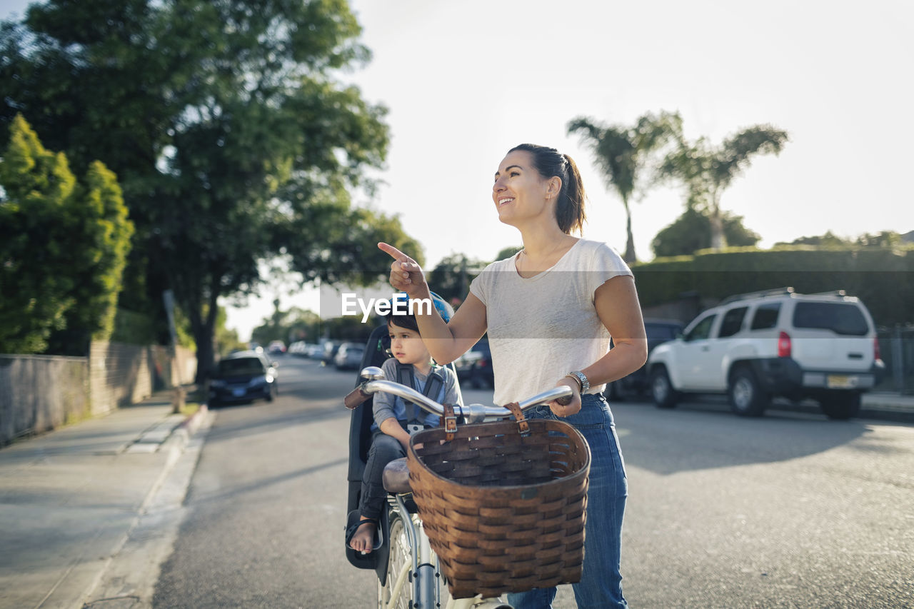 Happy woman gesturing while son sitting on bicycle outdoors