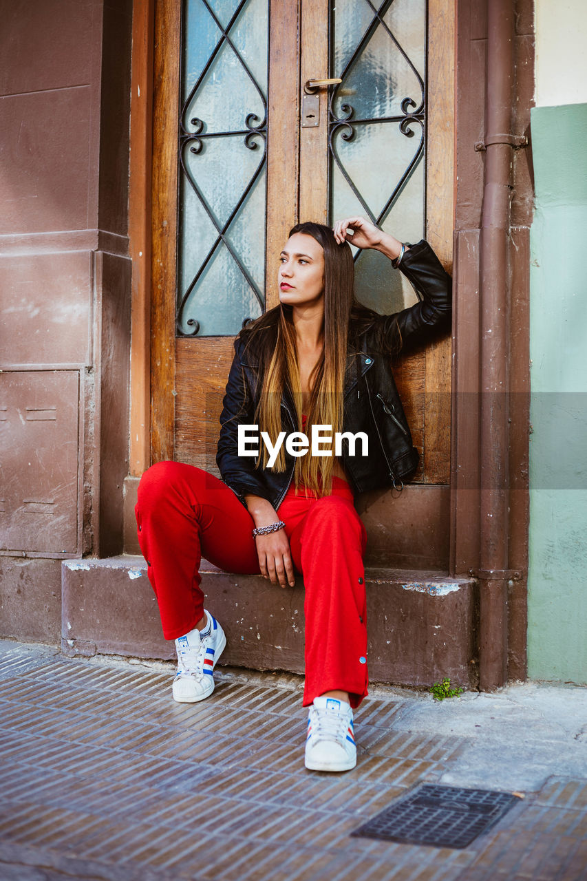 Full length of young woman looking away while sitting at entrance