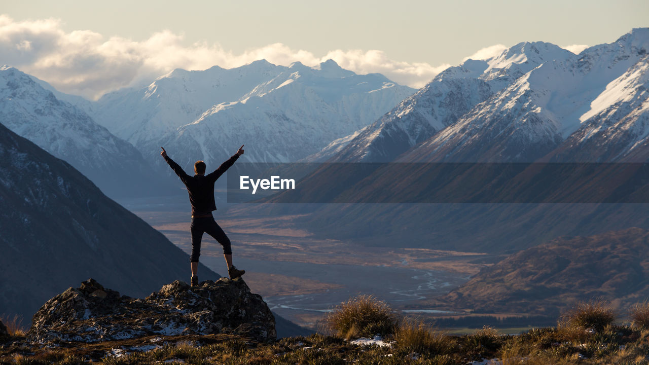 Rear view of hiker with arms raised looking at view while standing on cliff