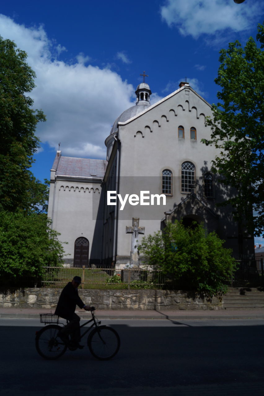 Side view of silhouette man riding bicycle on street by church in city