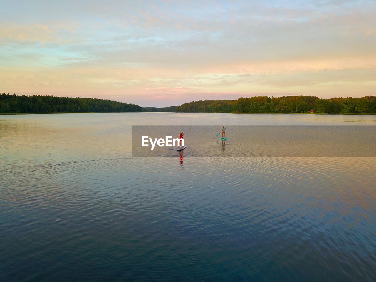 PEOPLE ENJOYING IN LAKE AGAINST SKY DURING SUNSET