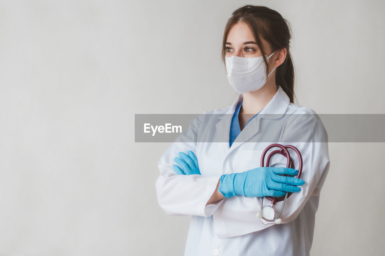 Doctor looking away while standing with stethoscope against white background