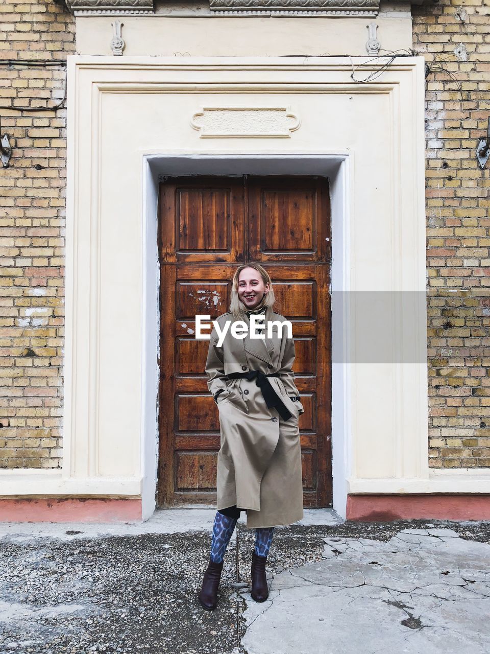 PORTRAIT OF A SMILING YOUNG WOMAN STANDING AGAINST DOOR