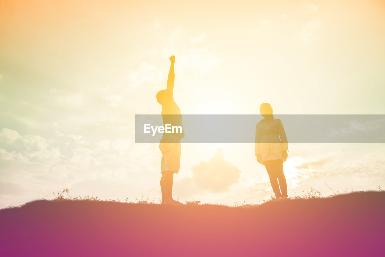 REAR VIEW OF SILHOUETTE WOMEN STANDING ON FIELD AGAINST SKY