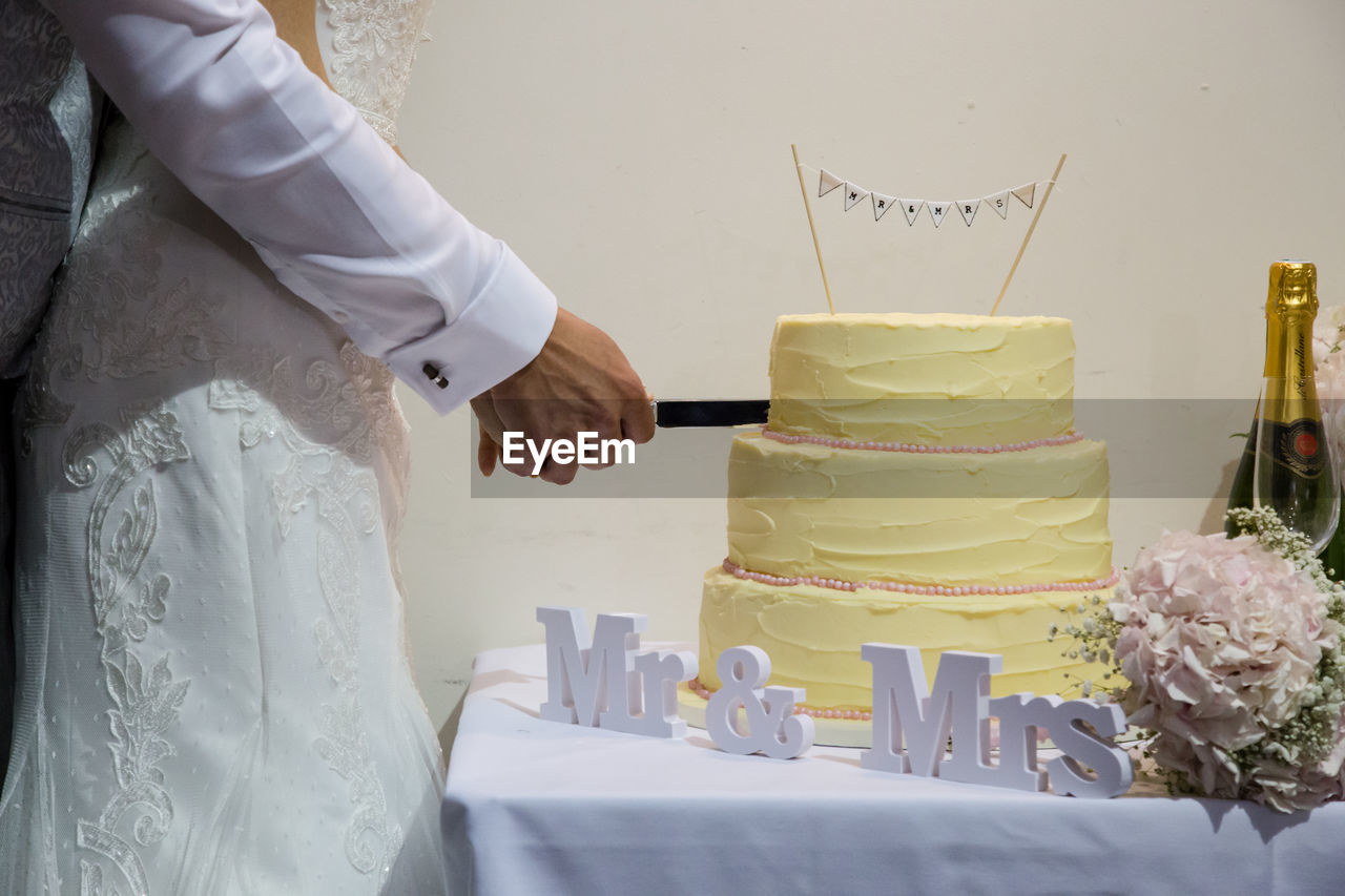 Midsection of couple cutting cake at table