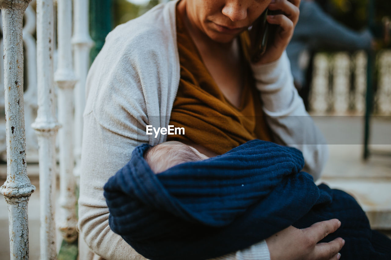 Midsection of woman with baby boy standing by fence