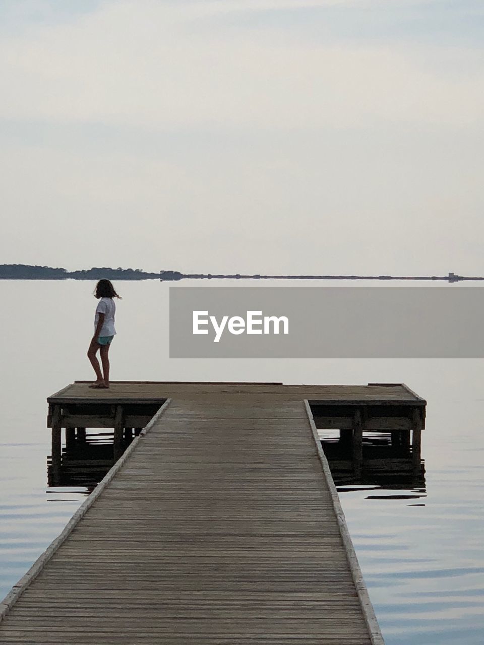 Girl standing on pier by lake against sky