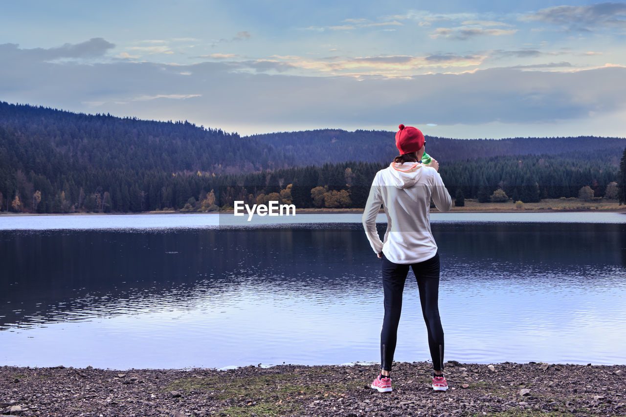 FULL LENGTH REAR VIEW OF MAN STANDING BY LAKE AGAINST SKY