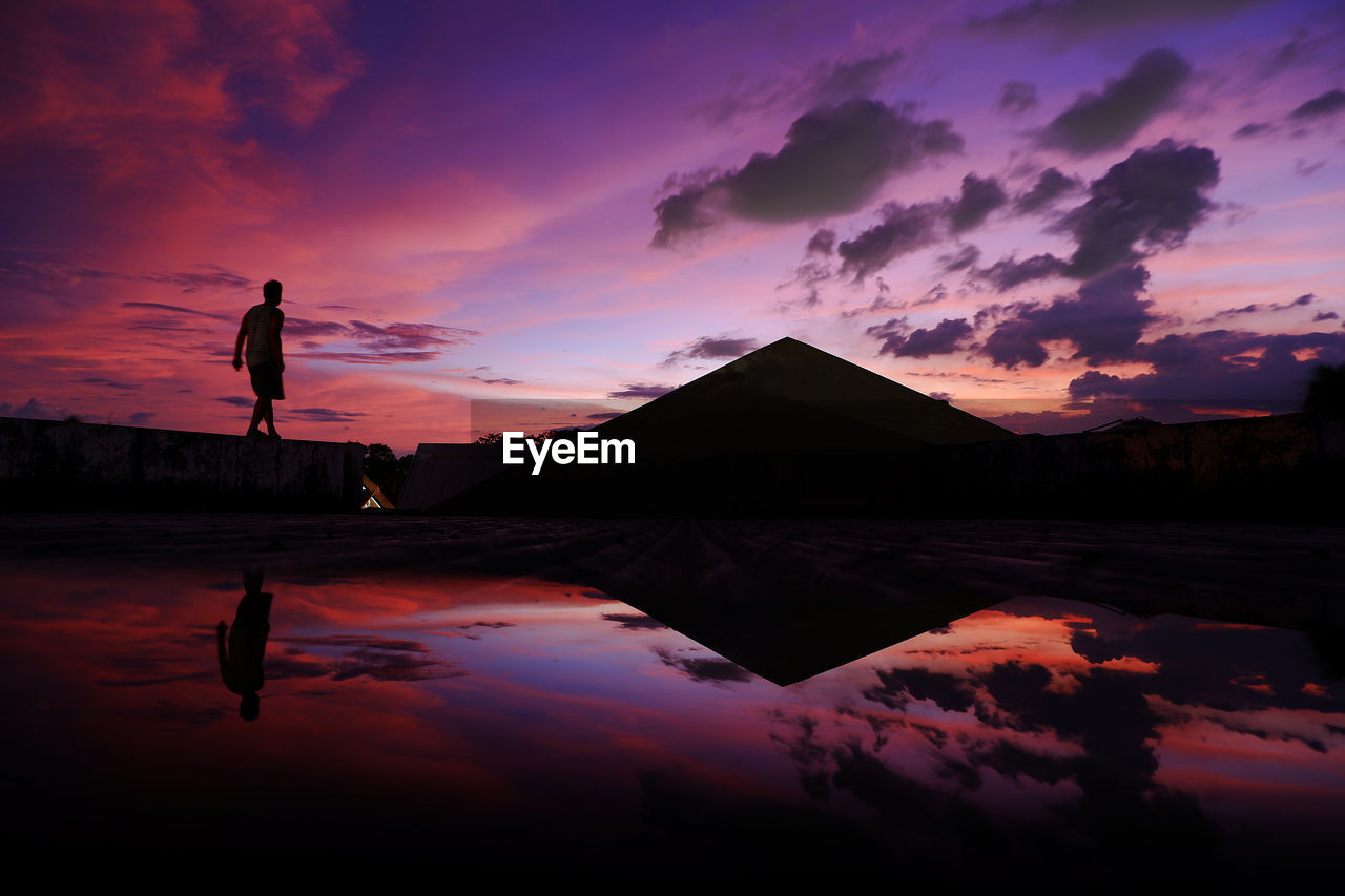 REFLECTION OF SILHOUETTE PERSON IN LAKE AGAINST SKY DURING SUNSET