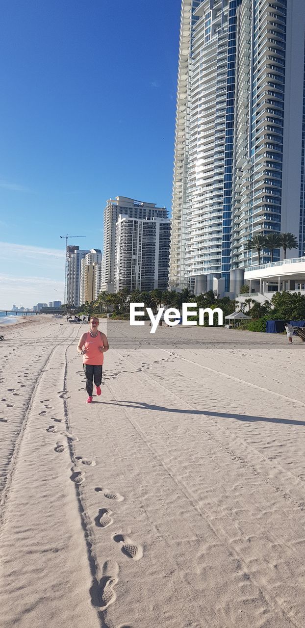 Full length of woman running on sand at beach in city